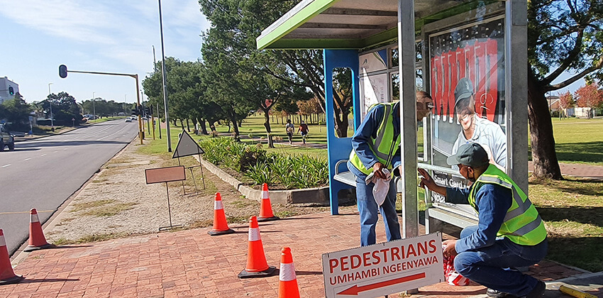 Workmen installing new glass panels on a GO GEORGE bus shelter.