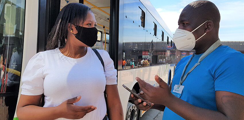 A man wearing a GO GEORGE identity card talking to a woman who is about to board a GO GEORGE bus.