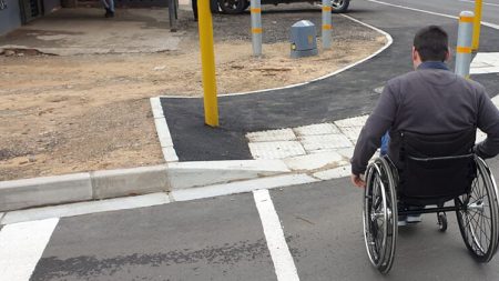 A person in a wheelchair crossing the street at a pedestrIan crossing, approaching a dropped kerb in the sidewalk.