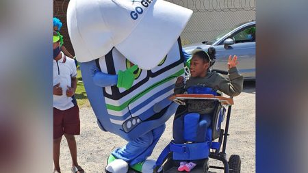 A mascot resembling the front of a bus is dancing with a young girl in a wheelchair.