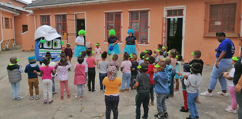 A group of toddlers listening to GO GEORGE staff and the mascot Georgie.