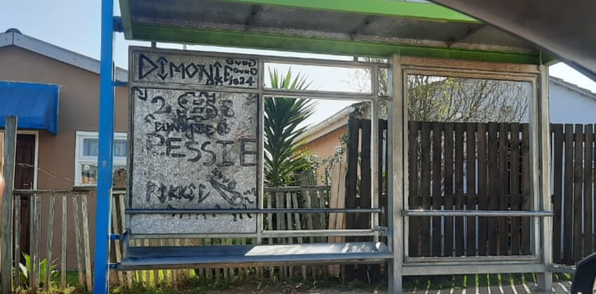 A GO GEORGE bus shelter with no panels except for an aluminium panel full of grafitti. 
