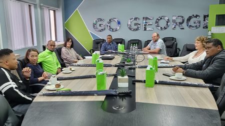 A group of people in discussion around a boardroom table with the name GO GEORGE on the wall behind them.