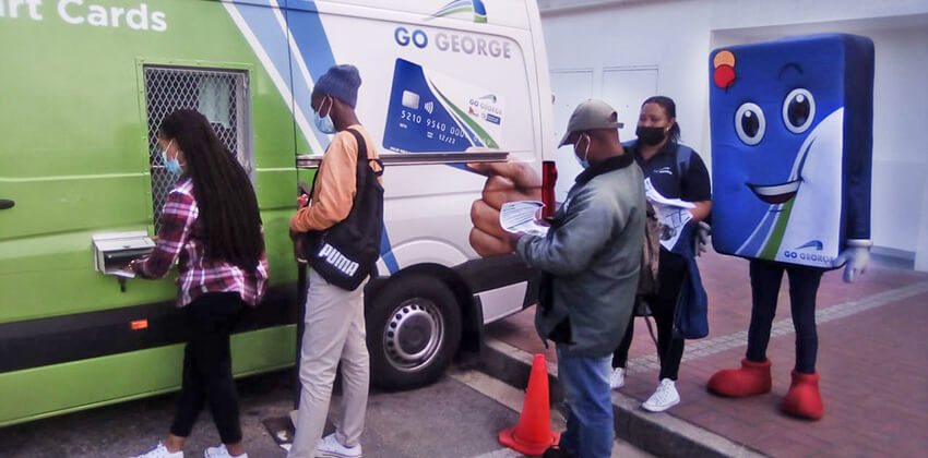 People standing in a short queue at a GO GEORGE-branded minibus where they top up their Smart Cards with trips.