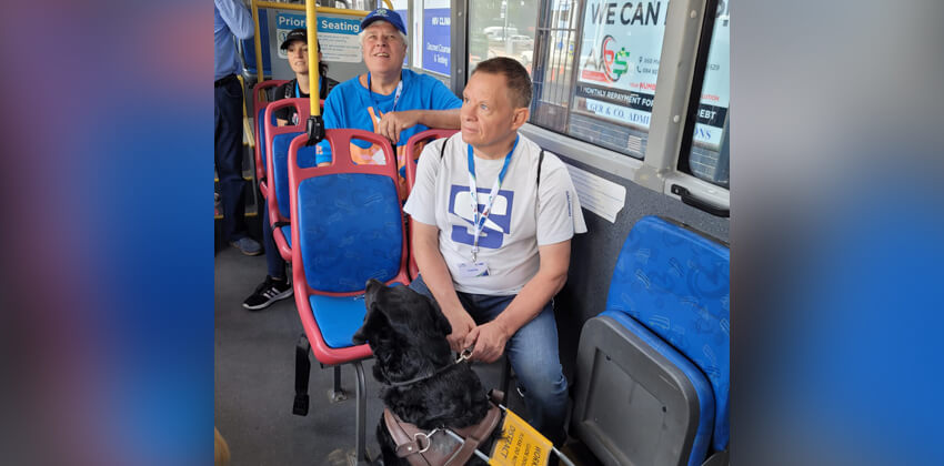 Aman with his black Labrador guide dog sitting in the bus.