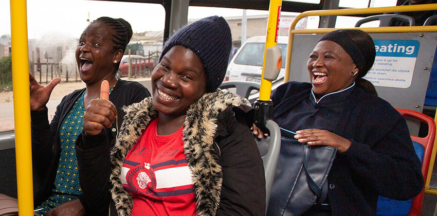 Passengers on a bus smiling and looking very happy.