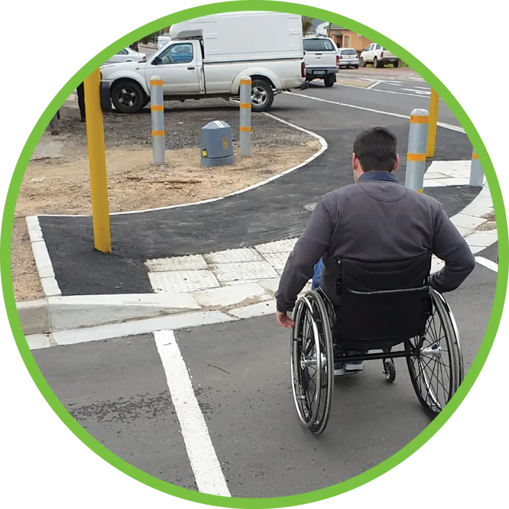 A man in a wheelchair crossing a street at a pedestrian crossing, approaching a lowered sidewalk built to accommodate wheelchairs.