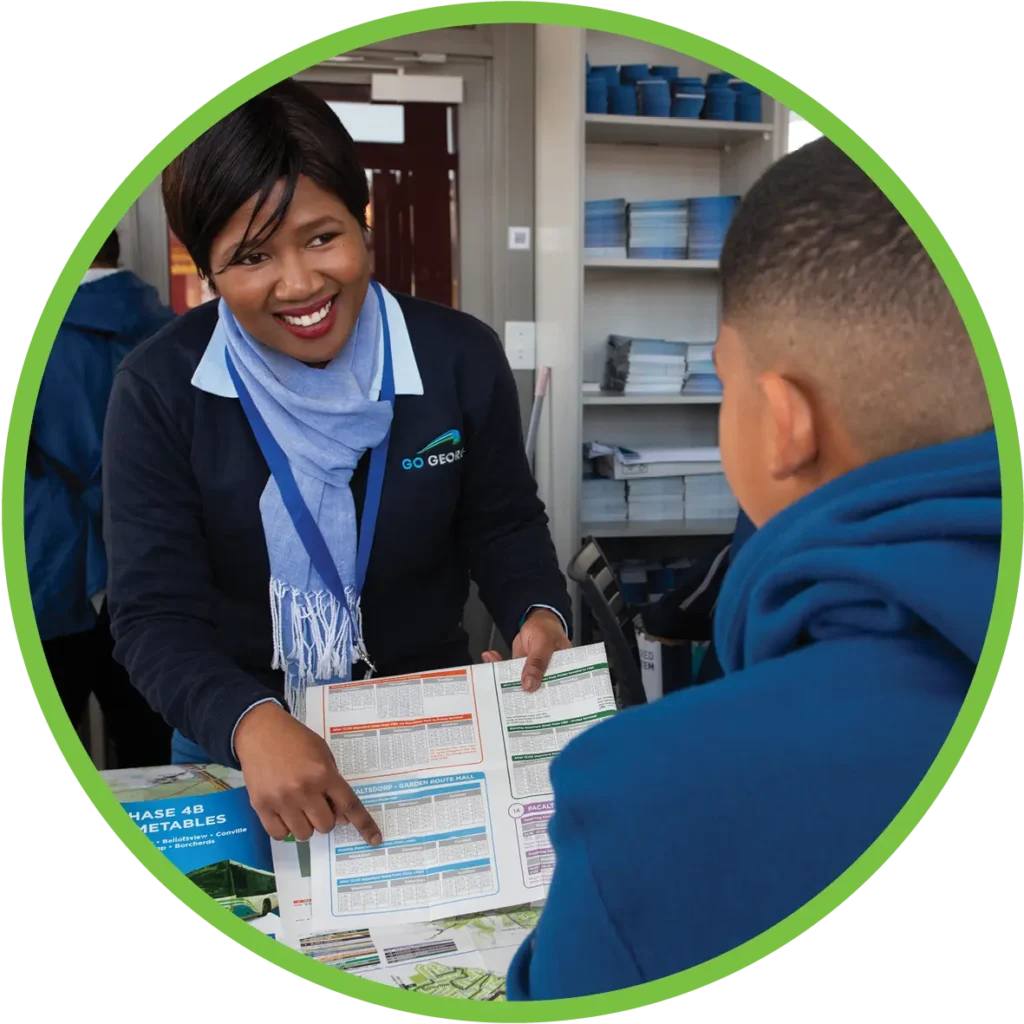 A woman inside an info kiosk helping a young student with trip planning through the window.
