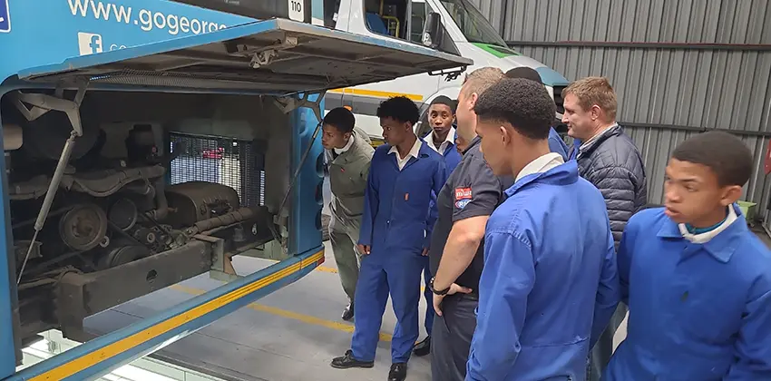 A group of teenage boys looking into a bus engine.