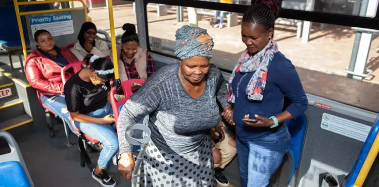 A person helping a woman with crutches to be seated in the bus.